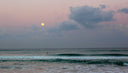A photo of the full moon after sunset and the ocean with waves, representing spring tides.