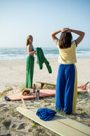 Two women on a beach with surfboards and wearing the Atmosea apres surf pants in blue and yellow. 
