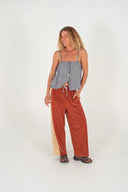 A model in a studio wearing the Atmosea Après Surf Panel Pants in rust brown cotton terry with cream side panels, a relaxed wide-leg silhouette, and adjustable drawstring waist.