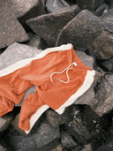 The Atmosea Après Surf Panel Pants in rust brown cotton terry with cream side panels, a relaxed wide-leg silhouette, and adjustable drawstring waist outside. 