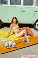 A model in the sun wearing the Atmosea Après Surf Panel Pants in rust brown cotton terry with cream side panels, a relaxed wide-leg silhouette, and adjustable drawstring waist.