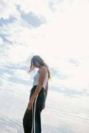 A side view of a model outside wearing the Atmosea Après Surf Pants in forest green cotton terry towelling with a relaxed wide-leg fit, elastic drawstring waist, and sporty canvas side stripes.