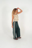 A side view of a model wearing the Atmosea Après Surf Pants in forest green cotton terry towelling with a relaxed wide-leg fit, elastic drawstring waist, and sporty canvas side stripes.