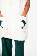 An upclose view of the front pocket of the Atmosea Delfi Après Surf Robe made from plush cotton terry towelling with a zip front, oversized hood, front pockets, and dolphin embroidery.
