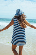 The back of a woman at the beach wearing the Atmosea Horizon Crochet Hat featuring colorful hand-crocheted cotton stripes and a wide brim for sunny beach days.