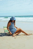 A woman at the beach wearing the Atmosea Horizon Crochet Hat featuring colorful hand-crocheted cotton stripes and a wide brim for sunny beach days. 