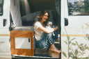 A woman outside in a van wearing the Atmosea Patchwork Pants in Turquoise Check featuring a relaxed wide-leg fit and colorful checkered cotton fabric.