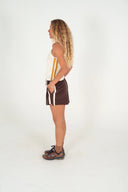 A side view of a model in a studio wearing the Atmosea Terry Towelling Après Surf Shorts in chocolate brown cotton terry with an elastic drawstring waistband and sporty side stripes.