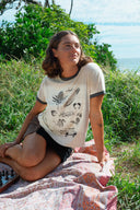 A model outside wearing the Atmosea Yaz Artifacts Ringer Tee in sand with dark grey contrast trim and original surf-inspired illustrations by artist Yaz Ward.