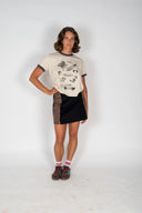 The front view of a model wearing the Atmosea Yaz Artifacts Ringer Tee in sand with dark grey contrast trim and original surf-inspired illustrations by artist Yaz Ward.