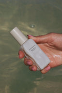 Bottle of Beachwashed Deep Current Treatment Oil held outdoors in natural sunlight.
