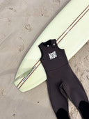 Flat lay of the Inner Relm Drop Knee Long Jane 2mm displayed beside a surfboard.