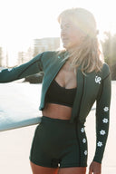Model wearing the Inner Relm Green Envy Vest 2mm in a coastal setting with ocean views.