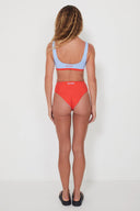 A model wearing the Salt Gypsy Drifter 2.0 reversible swim bottoms in Baby Blue and Chilli Red from the back