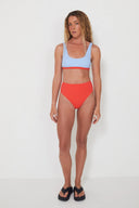 A model wearing the Salt Gypsy Drifter 2.0 reversible swim bottoms in Baby Blue and Chilli Red from the front