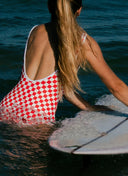 A model in the water wearing the Salt Gypsy Everyday One Piece in Chilli Checkers from the back