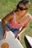 A surf model waxing her surfboard in the Salt Gypsy Everyday One Piece in Chilli Checkers