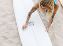 Surfer applying Salt Gypsy Premium Eco Surf Wax - All Water to a surfboard before a session.
