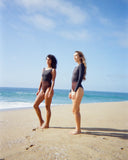 Model wearing Seea Madi Surf Suit in Black/Cappuccino on the beach