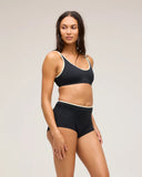 A model wearing the Seea Maggie Bikini Top in Black featuring textured recycled bouclé fabric, adjustable straps, and supportive bralette design.
