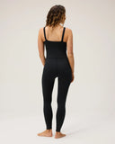 The back view of a model wearing the Seea Penelope Bodysuit in Black featuring full-length surf leggings, adjustable straps, and recycled C-Skin fabric.