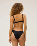 The back view of a model wearing the Seea Phoebe Bikini Bottom in Black featuring textured recycled fabric, high-cut hips, and cheeky coverage.