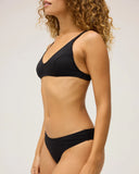A model wearing the Seea Phoebe Bikini Bottom in Black featuring textured recycled fabric, high-cut hips, and cheeky coverage.