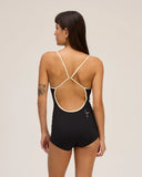 The back view of a model in a studio wearing the Seea Rosita One Piece swimsuit in Black featuring white contrast trim, adjustable straps, and a low scoop back.