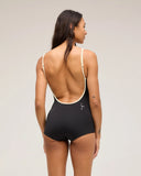 The back view of a model wearing the Seea Rosita One Piece swimsuit in Black featuring white contrast trim, adjustable straps, and a low scoop back in a studio.