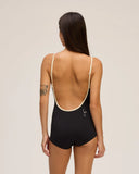 The back view of a model wearing the Seea Rosita One Piece swimsuit in Black featuring white contrast trim, adjustable straps, and a low scoop back.