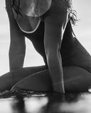A woman on a surf board in the Seea Rosita One Piece swimsuit in Black featuring white contrast trim, adjustable straps, and a low scoop back.