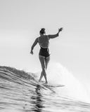 A woman surfing in the Seea Rosita One Piece swimsuit in Black featuring white contrast trim, adjustable straps, and a low scoop back.