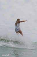 Model wearing Alaia Surf Suit in Aloha Dune Print while surfing