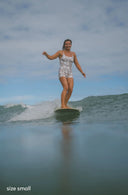 Model wearing Alaia Surf Suit in Aloha Dune Print while surfing
