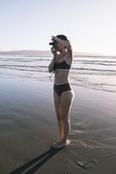 A woman holding a surfboard and wearing the September cold brew top and bottoms