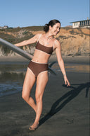 A woman holding a surfboard and wearing the September cold brew top