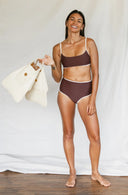 Front view of model wearing Island Bikini Bottom in Cold Brew while smiling and holding flippers