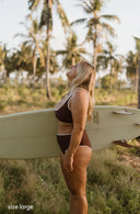 Model wearing Island Bikini Bottom in Cold Brew outside and holding a surfboard