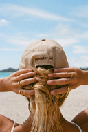 Model on the beach wearing the September The Line Barrel Dodger Dad Hat surf-inspired adjustable cap from the back