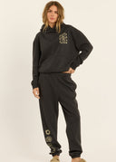 A model wearing the Sisstr Coast to Coast Fleece Jogger in Vintage Black featuring a relaxed fit, elastic waistband, cuffed ankles, and coastal-inspired leg graphics.