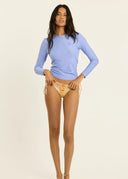A model posing and wearing the Sisstr Seeker Solid women’s surf rashguard in Blissful Blue