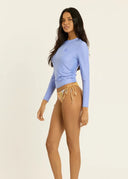 The side view of a model wearing the Sisstr Seeker Solid women’s surf rashguard in Blissful Blue