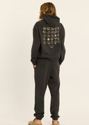 The back view of a model wearing the Sisstr Surf Check Fleece Hoodie in Vintage Black featuring front and back graphic prints, relaxed fit, and kangaroo pocket.