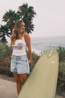 Model wearing the Sisstr Surfside Knit Tank with denim shorts and carrying a surfboard.