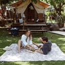 Two people relaxing on the Slowtide Hau Oversized Beach Blanket outdoors.