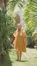 Model wearing the Sunward Bound Hooded Changing Towel in Turmeric in a sunny outdoor setting.