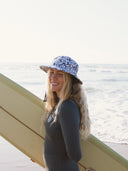 Model wearing the Sunward Bound Vintage Juju Surf Hat UPF50+ while carrying a surfboard on the beach.